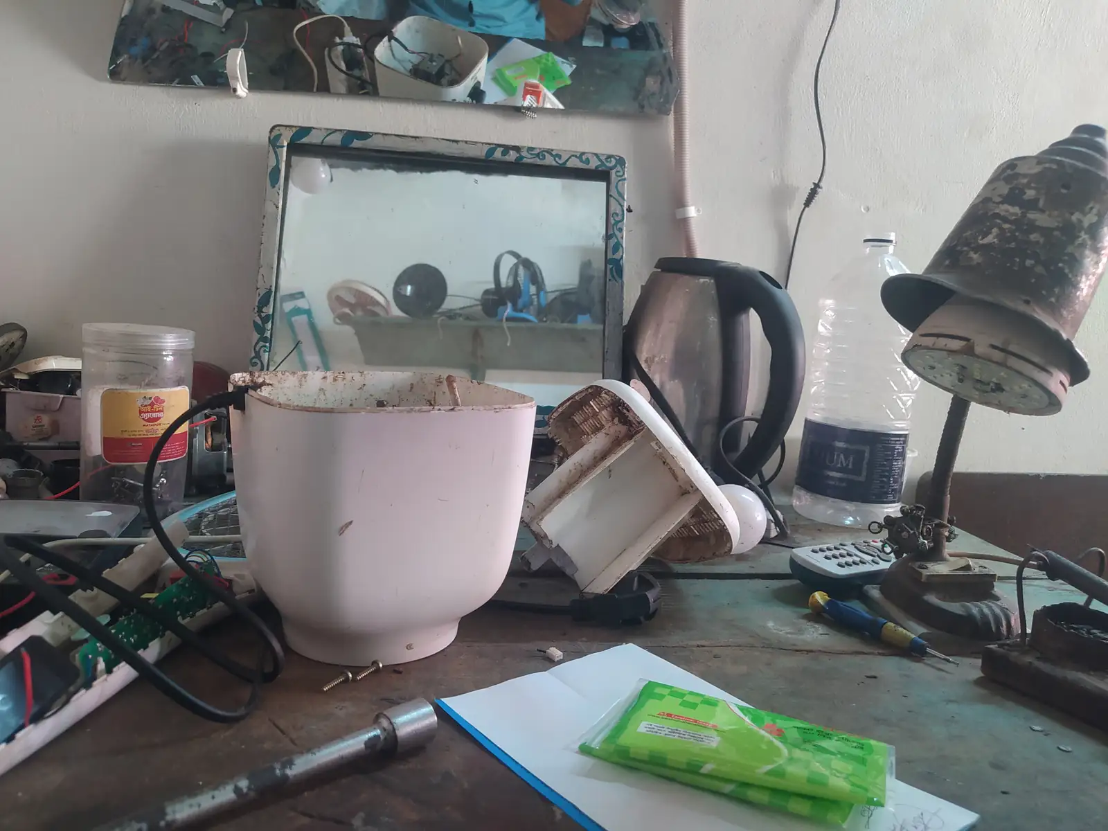 A cluttered electronics component counter in Bangladesh, trays of parts and tools spread across the table.