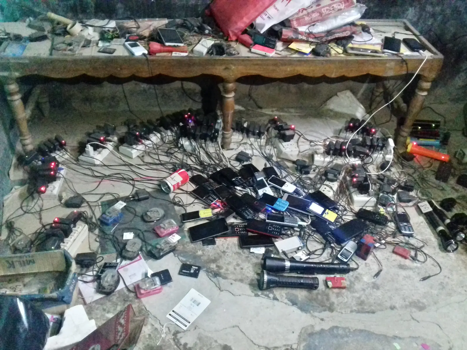 A small mobile-phone charging and repair shop in a village market in Bangladesh, handsets laid out on the counter.